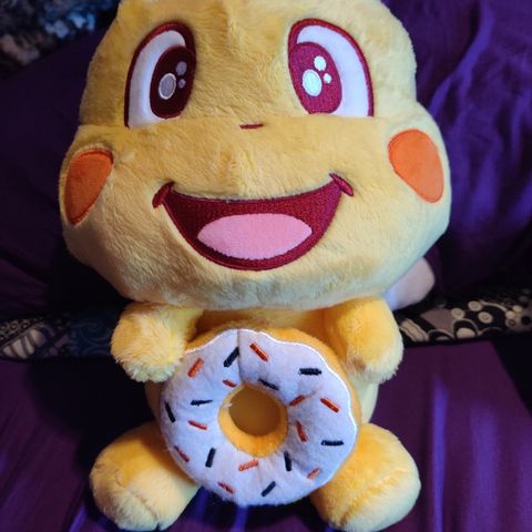 A QooBee plushy hugging a donut on a purple blanket
